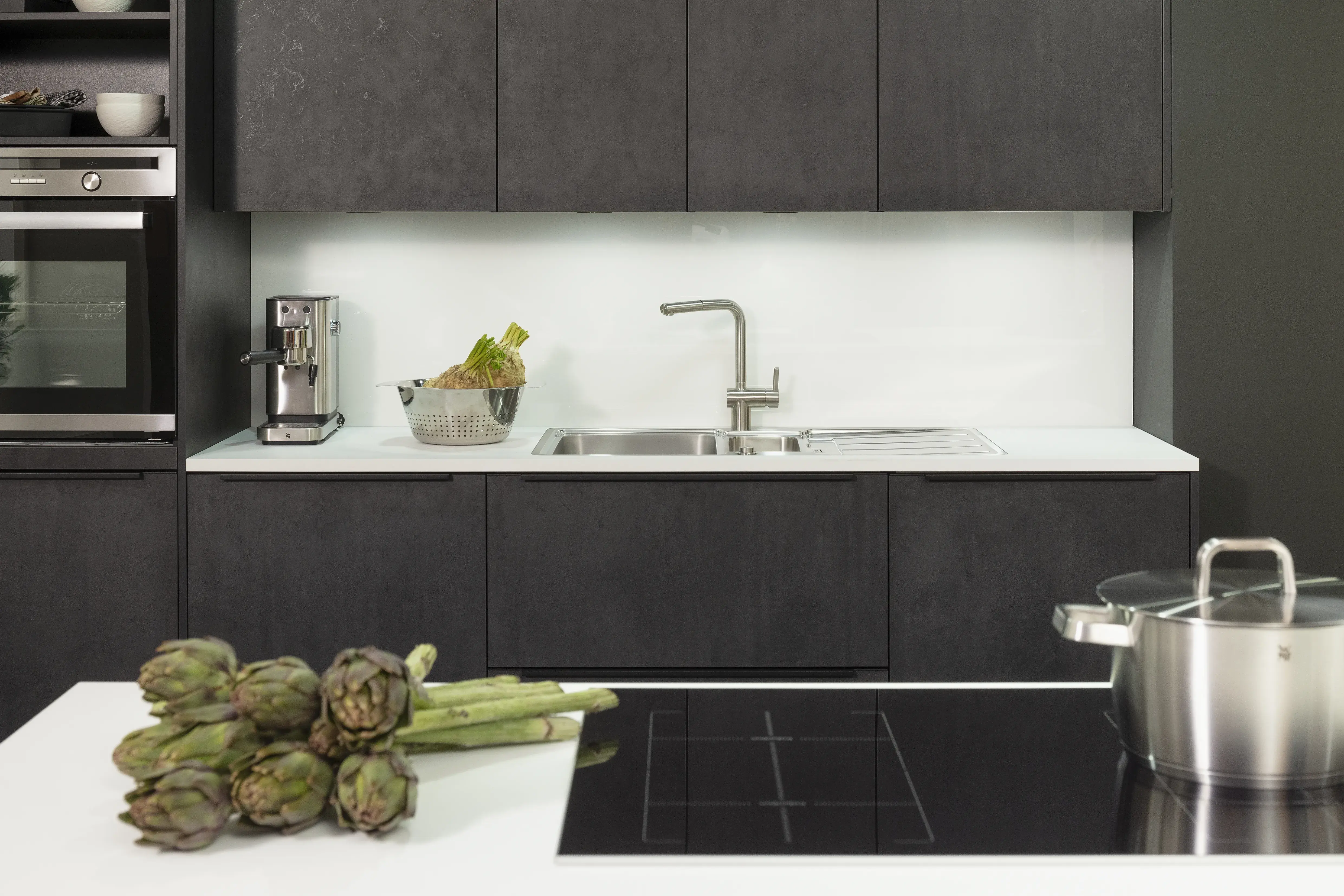 Küchenzeile in Beton-Dekor mit Spüle sowie integriertes Kochfeld im Vordergrund. 